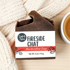 Handcrafted fall soap bar with 'Fireside Chat' packaging on a wooden surface with a knitted blanket.