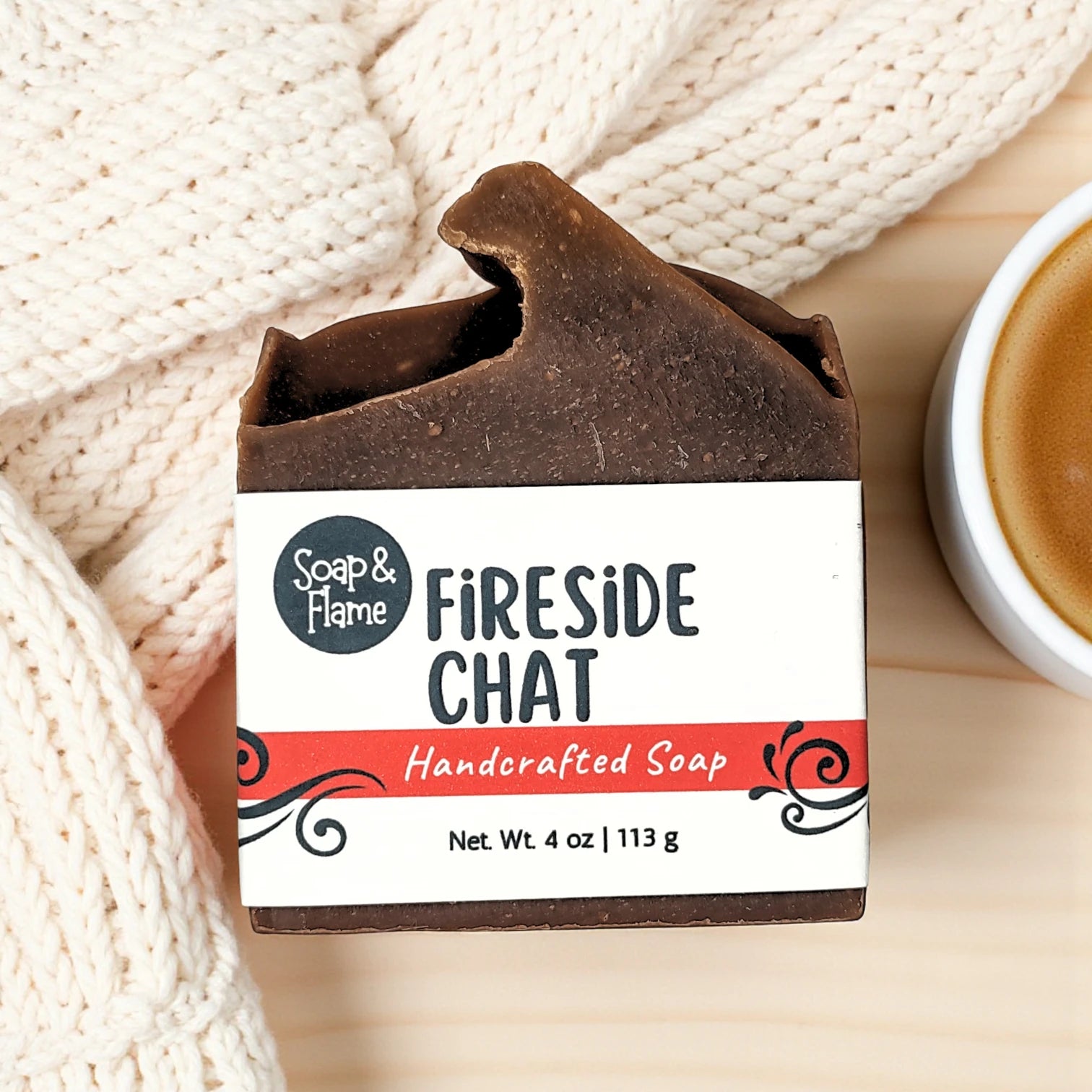 Handcrafted fall soap bar with 'Fireside Chat' packaging on a wooden surface with a knitted blanket.