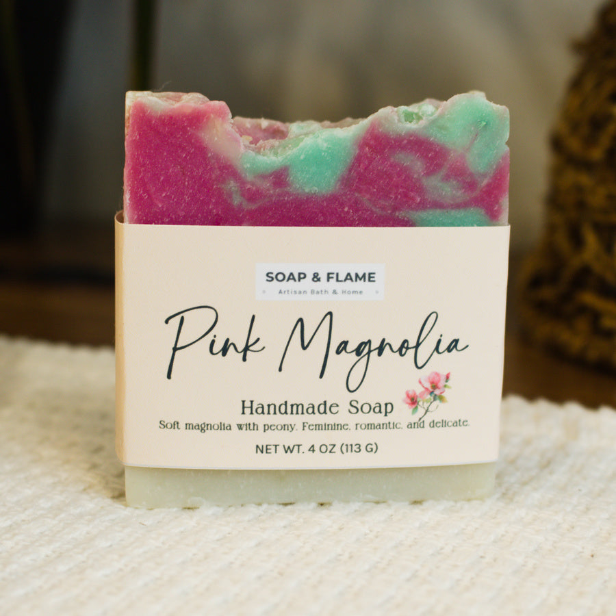 Handmade soap bar with 'Pink Magnolia' label by Soap & Flame on a textured surface.