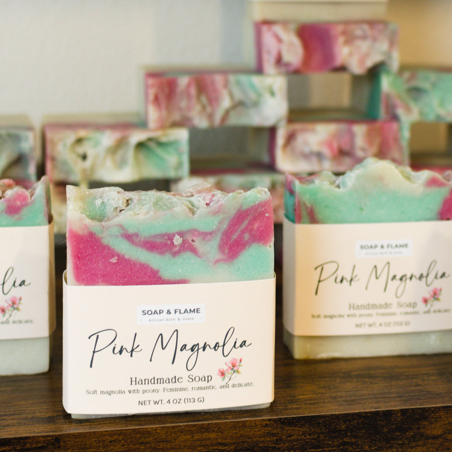 Handmade soap bars with 'Pink Magnolia' packaging on a wooden surface.