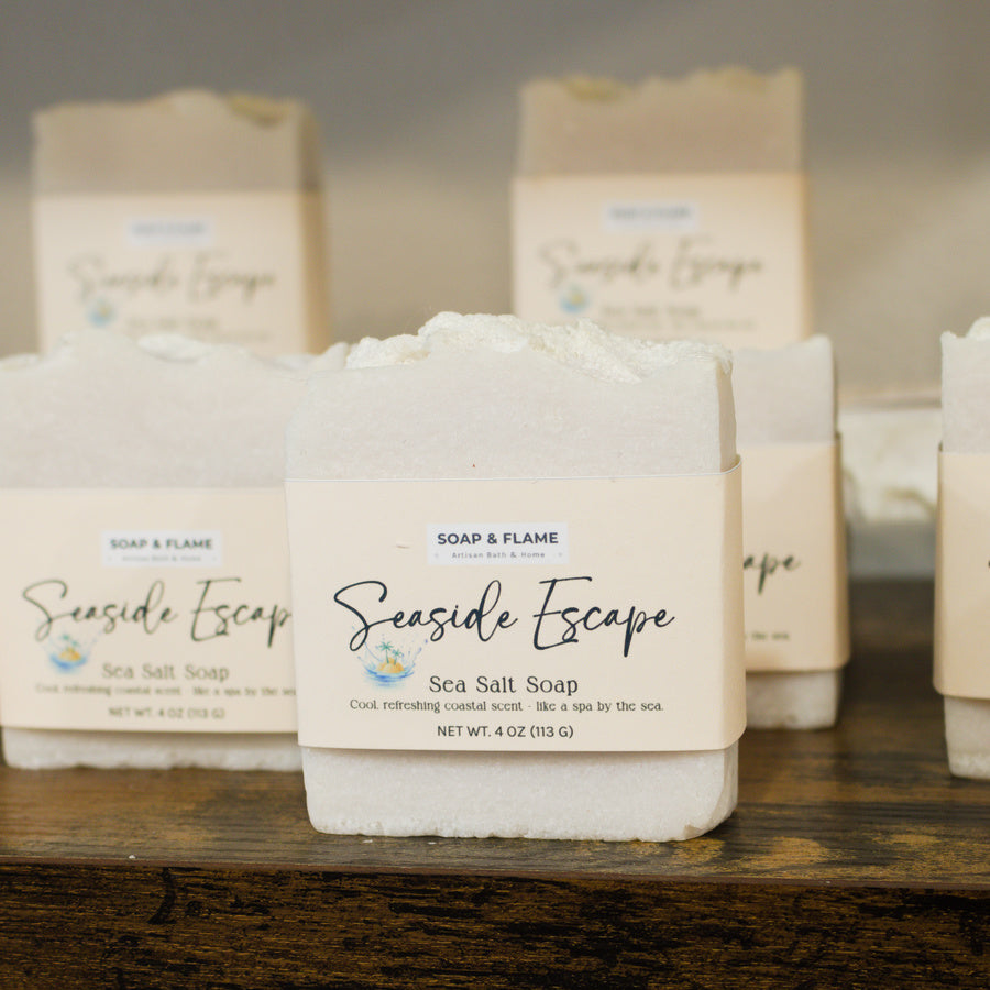 Sea Salt Soap labeled 'Seaside Escape' by Soap & Flame on a wooden surface with a blurred background.
