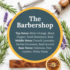A circular graphic with the text 'The Barbershop' and fragrance notes, surrounded by barbershop-themed props including a shaving brush, metal shaving tool, lavender sprigs, rosemary branches, a leather block, and a dried orange slice on a light marble background.