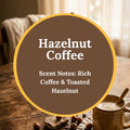 Hazelnut Coffee Handcrafted Soap scent infographic: a mug of coffee with hazelnuts scattered on a rustic wooden table beside a sunlit window, with text reading Hazelnut Coffee, Scent Notes: Rich Coffee & Toasted Hazelnut.
