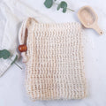 Natural Sisal Soap Bag: a cream sisal drawstring pouch in a flat lay with a wooden scoop, eucalyptus sprigs, folded cloth, and scattered sea salt.