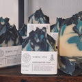 Handcrafted Nordic Pine scented soap bars with white paper labels, displayed on a dark wooden surface against a light wall.