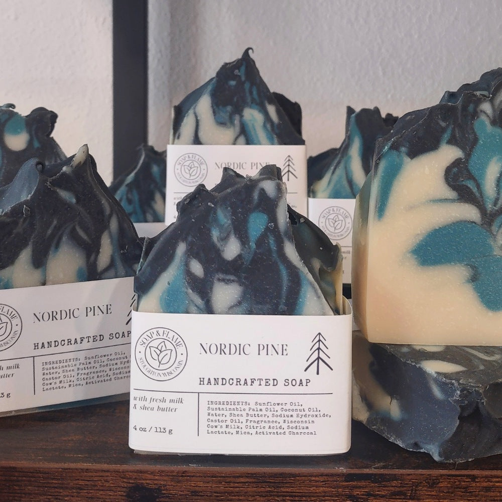Handcrafted Nordic Pine scented soap bars with white paper labels, displayed on a dark wooden surface against a light wall.
