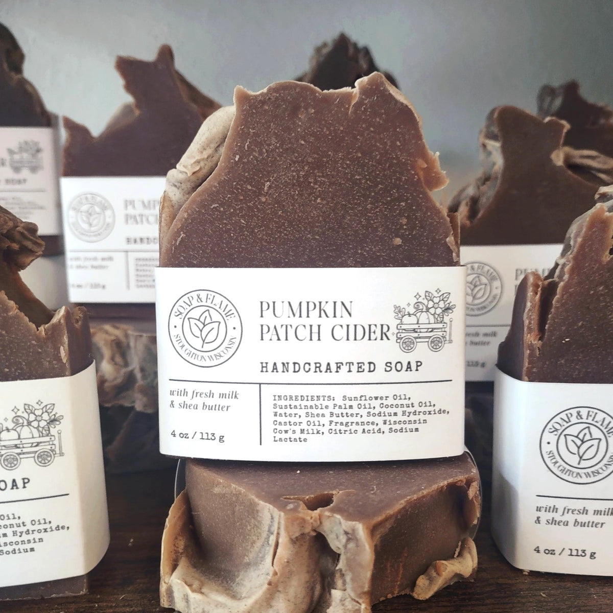 Row of handcrafted Wisconsin milk soap bars with a rustic brown mountain-peak texture, each wrapped with a white paper label, arranged on a wooden surface.