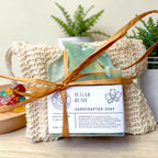 Sugar Rush Essentials Gift Set: a blue swirled soap bar tied with raffia in a natural sisal bag, surrounded by colorful candy pieces on a wood surface.