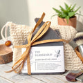 The Barbershop Essentials Gift Set: a charcoal soap bar tied with raffia in a natural sisal bag, styled with a wooden shaving brush and a small wood bowl against a dark background.